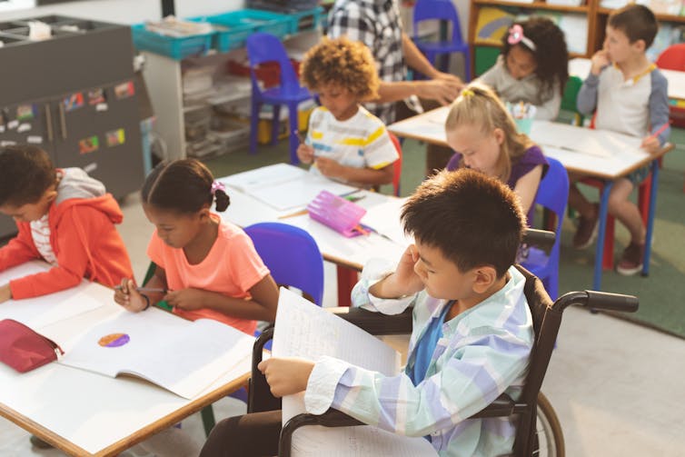 Young students in a classroom working at desks; one is in a wheelchair.