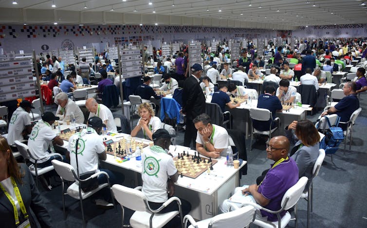 A large room full of people sitting at tables playing chess.