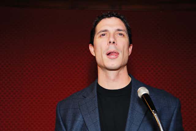 A man in front of a microphone with his tongue over to the side of his mouth