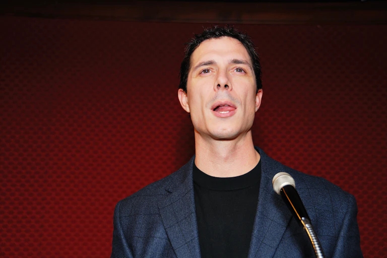 A man in front of a microphone with his tongue over to the side of his mouth