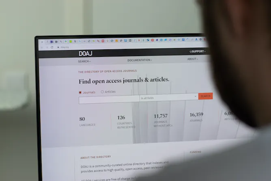 Profil seseorang yang melihat layar komputer yang menunjukkan bilah pencarian untuk jurnal dan artikel akses terbuka