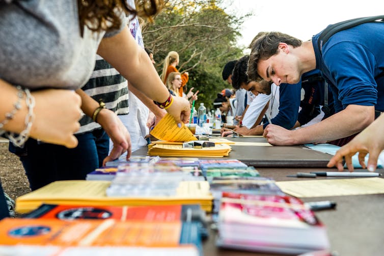 Students seen at a table with brochures outdoors.