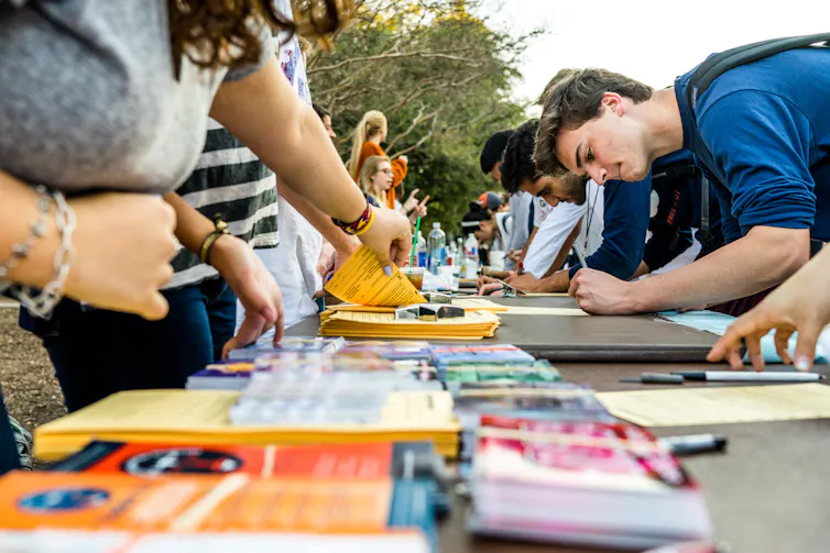 Students seen at a table with brochures outdoors.