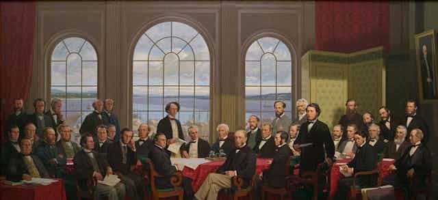 A painting shows a room full of men, some bearded, in bow ties and jackets in a room overlooking a body of water. 