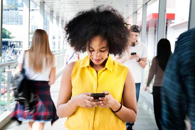 Young woman in a yellow top using a smartphone in the middle of a walking crowd.
