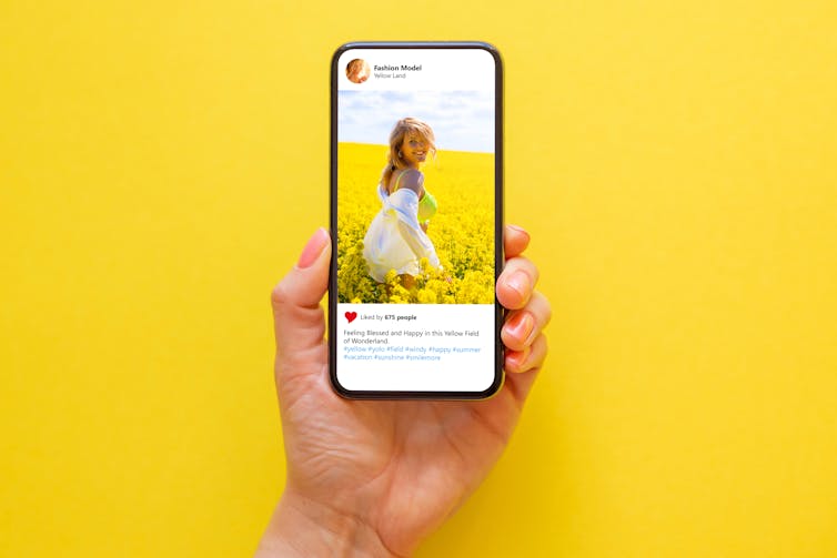 A hand holding up a phone screen against a yellow background.
