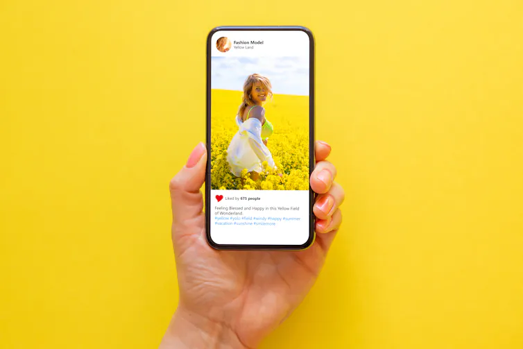 A hand holding up a phone screen against a yellow background.