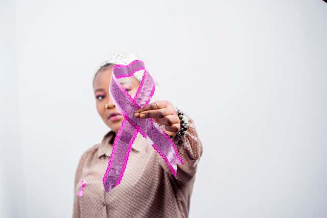 A woman wearing a pink shirt holds up a pink ribbon