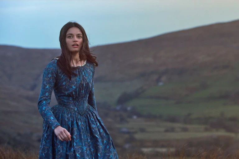 A young dark-haired woman in Victorian dress standing on a moor. dress