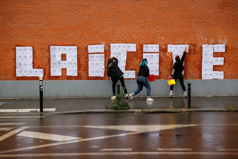 Trois militantes féministes font un collage sur un mur à Montreuil le 20 octobre 2020 lors d'un événement hommage à la rédaction de Charlie Hebdo.