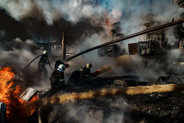Firefighters carry hoses amid debris, flames and smoke.