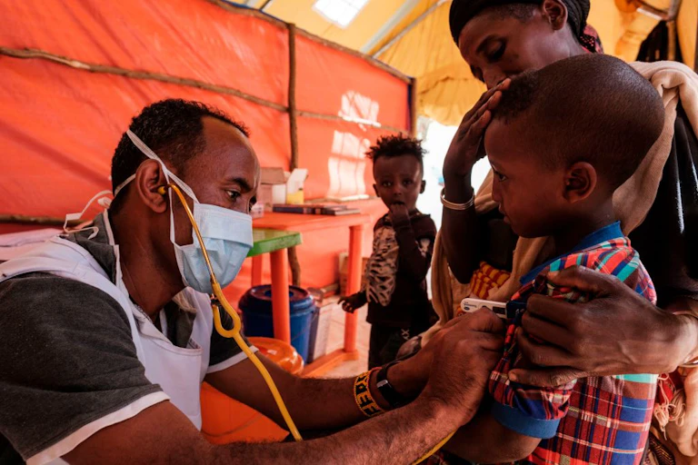 A healthworker examining a child as his mother holds him.