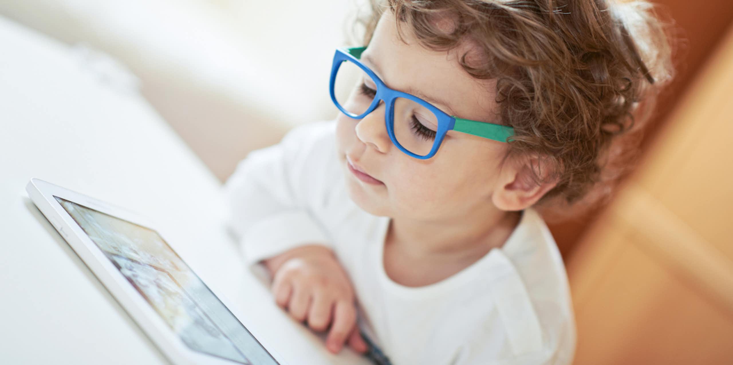 jeune garçon avec des lunettes regarde une tablette électronique