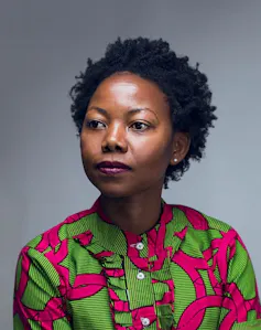 A young black woman in a red and green shirt staring off to the left.
