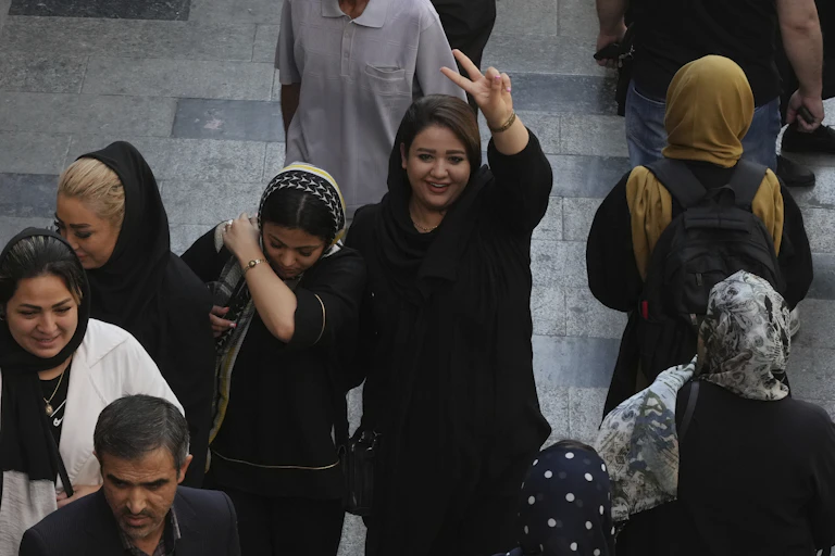 A dark-haired woman smiles and flashes a victory sign as she walks with other women in a bazaar.
