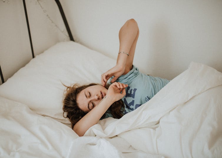 Photo d’une jeune femme qui s’étire dans un lit.
