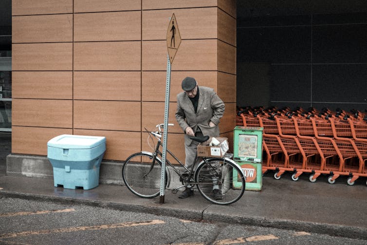 Un vieil homme s’apprête à détacher son vélo, accroché à un poteau dans la rue.
