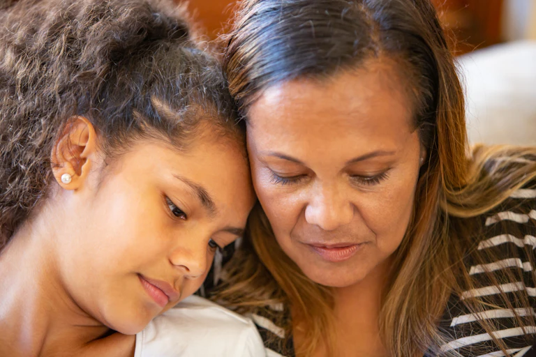 A parent sits with their child, their heads lean in together as they look down at something.
