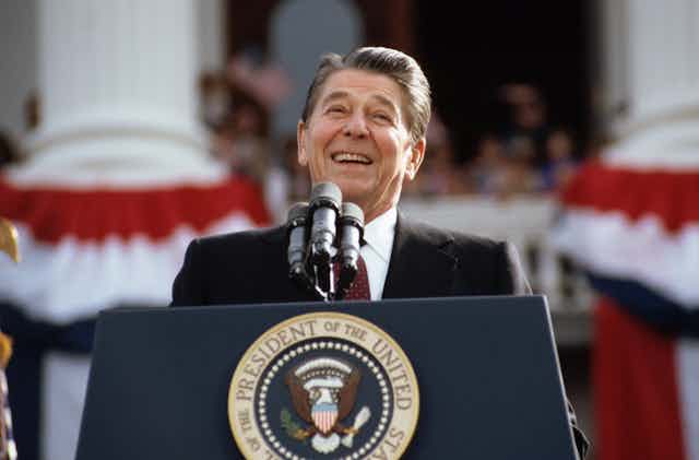 A smiling Ronald Reagan at a lectern bearing the U.S. presidential seal