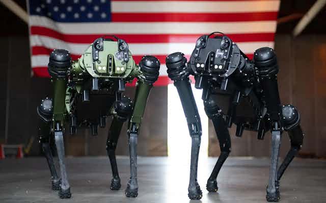 Two dog-like robots standing in front of the US flag