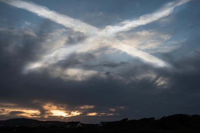 A stormy looking sky at sunset with two aeroplane contrails that look like the Scottish saltire.