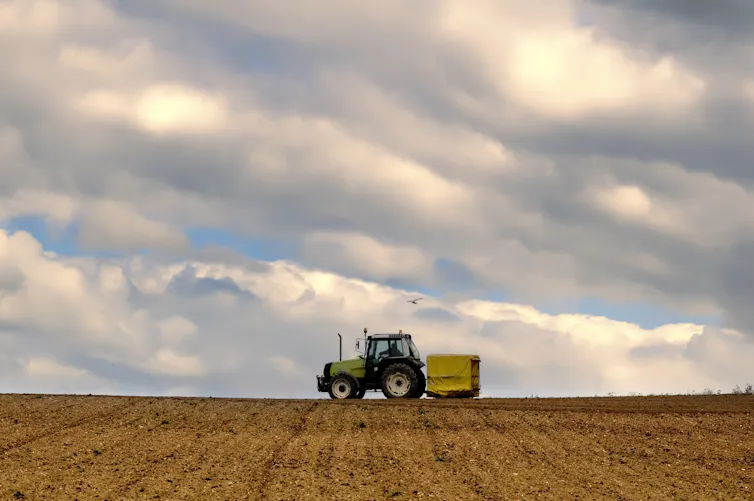 A tractor trundles along the horizon of a ploughed field.
