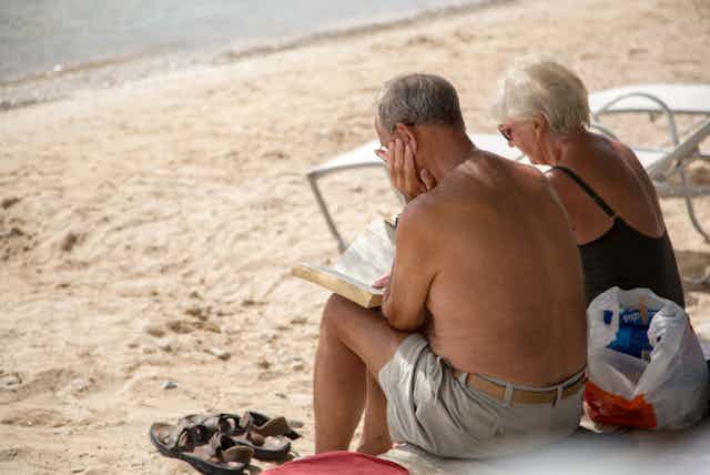 A retired couple sitting on a beach reading