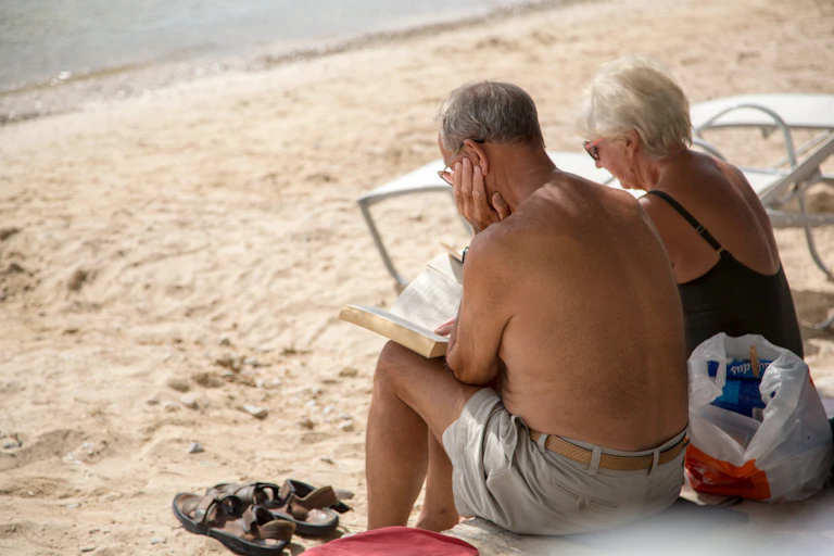 A retired couple sitting on a beach reading