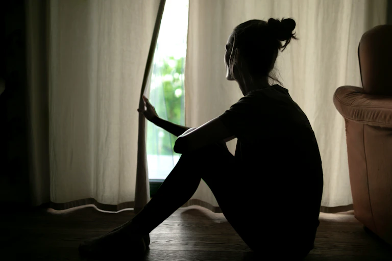 Une femme dans l'ombre entrouvre un rideau pour regarder dehors