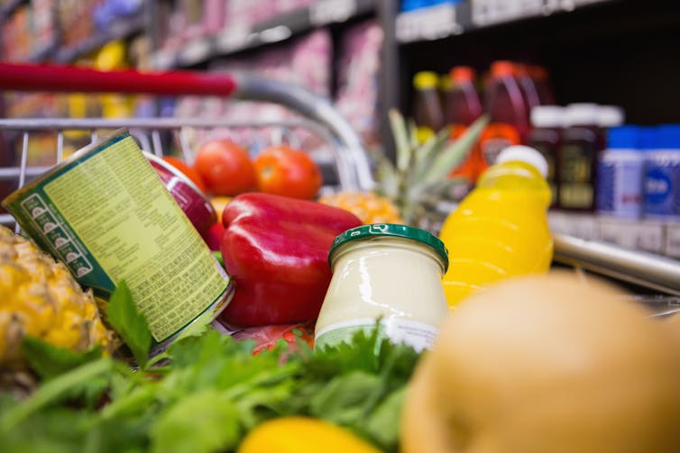 A shopping trolley filled with vegetables, tinned food and juice.