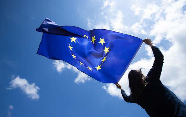 A person holding a European Union flag up to the sky.