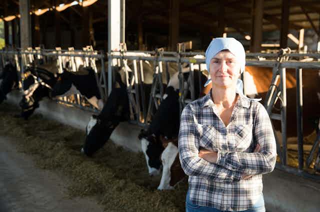 Mujer de brazos cruzados mira a cámara en un establo de vacas.
