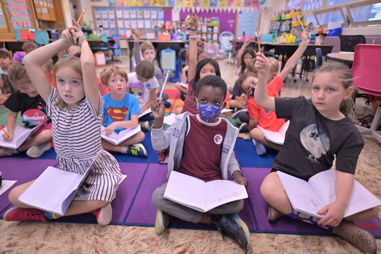 Students sit on the floor and raise their hands.