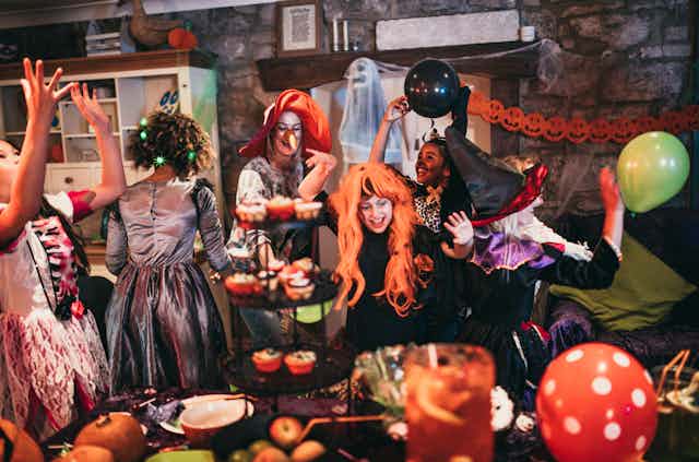 Group of young friends dressed in costumes dancing and playing together at a Halloween party.