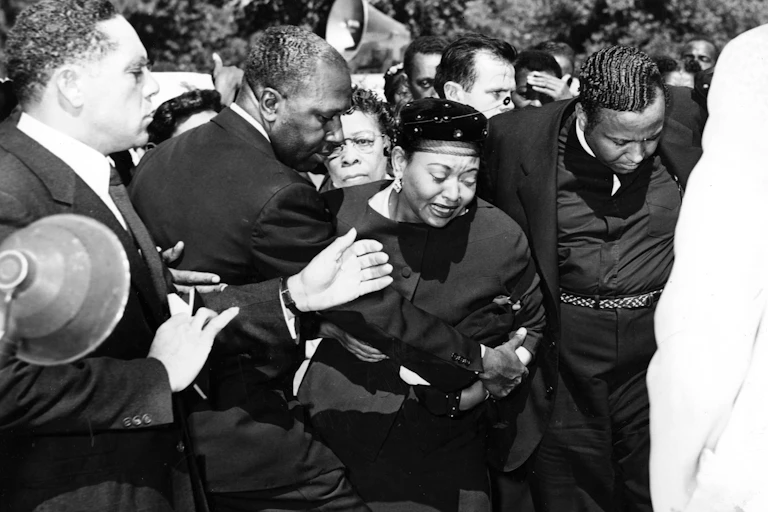 Distraught woman held by group of men.