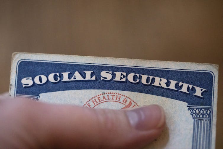 A white hand holds a card reading social security