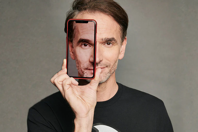 A man in a black t-shirt looking at the camera through a transparent phone case