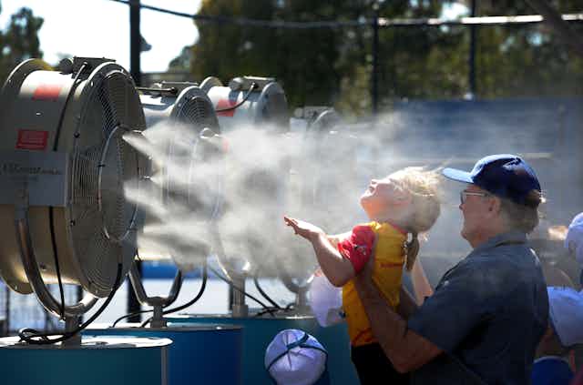 Man holds up young girl in front of a cooling mist fan