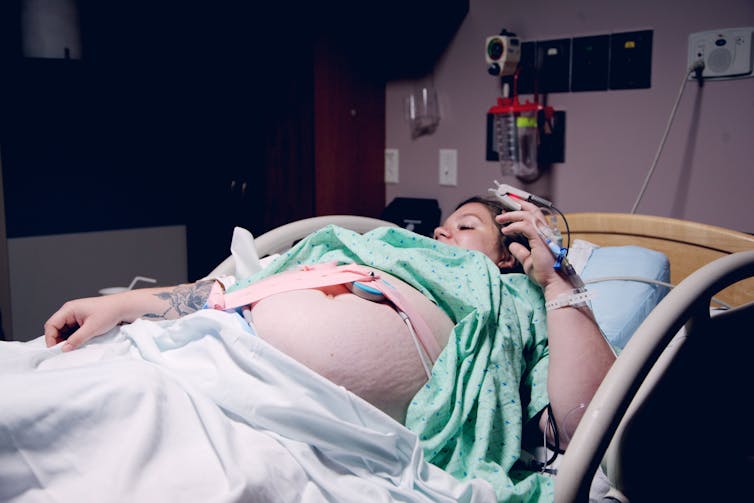 Pregnant woman lying in hospital bed with monitor around her abdomen.