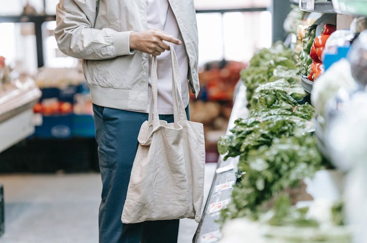 A customers holds a shopping bag while looking at vegetables.