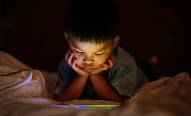 A child watch something on a device while lying on a bed