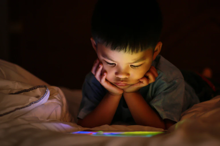 A child watch something on a device while lying on a bed