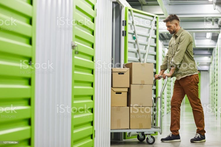 Man wheels a trolley of storage boxes into a rented storage unit.