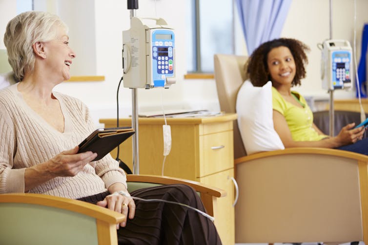 Two women in chairs beside medical equipment. One is middle-aged and one is young.