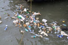 A cluster of plastic bottles and litter floating in brown water.