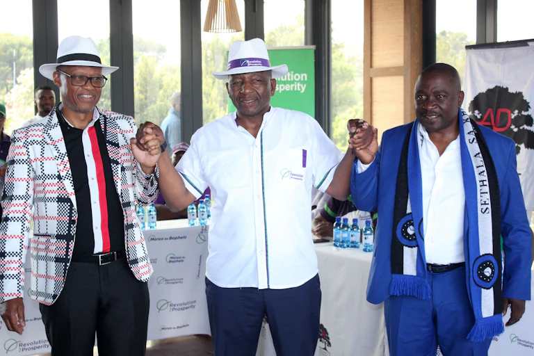 Three men, two of them wearing hats, hold up hands while standing.