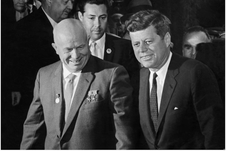 Two men in suits stand next to each other and smile