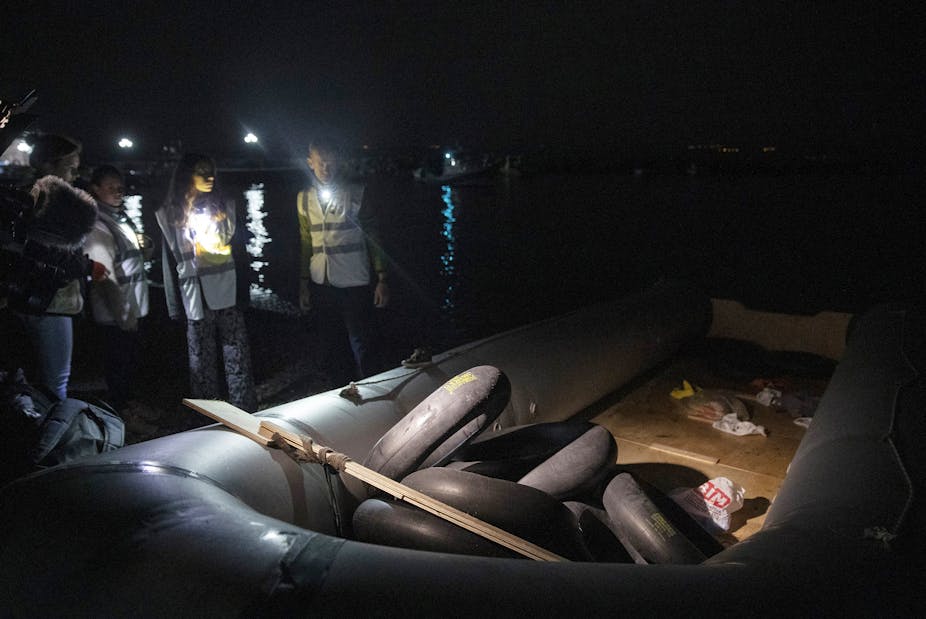 Frontex officials in high vis vests and carrying flashlights approach an empty rubber dinghy on the shores of a Greek island.