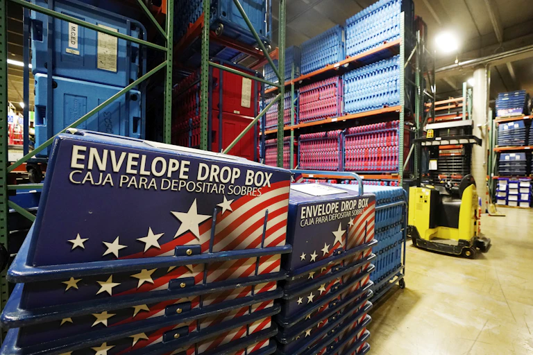 a sign reading Envelope Drop Box is visible in a warehouse with stacked bins in the foreground and shelves filled with stacked sandwich boards