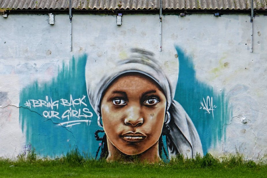A mural of a young woman in a head wrap, eyes gazing intently, painted on a wall.